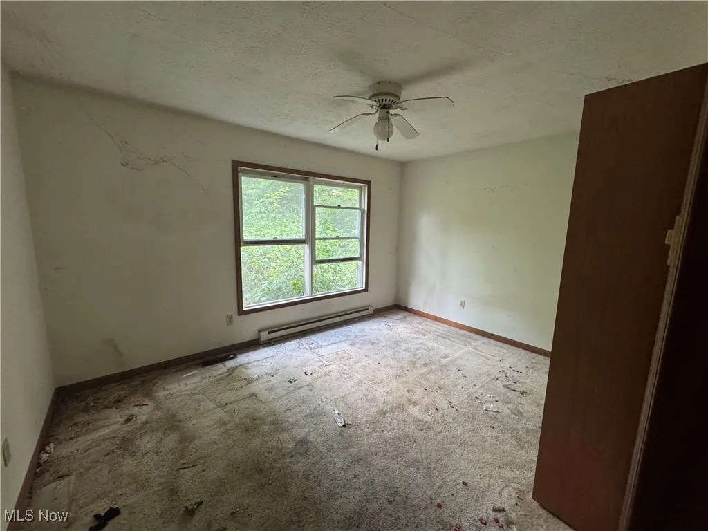 Carpeted spare room with a baseboard radiator, ceiling fan, and a textured ceiling