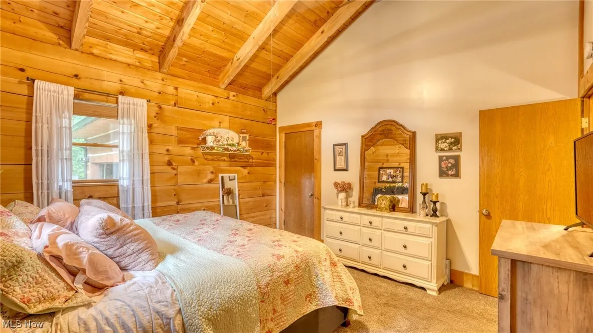 Bedroom featuring light carpet, wooden walls, a wood ceiling with exposed beams, and high vaulted ceiling