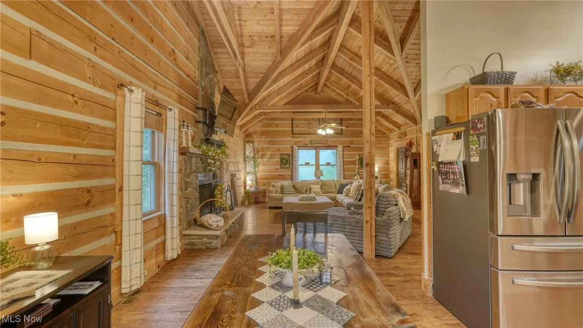 Living room with a wood ceiling with exposed beams, light wood finished floors, wood walls, and high vaulted ceiling