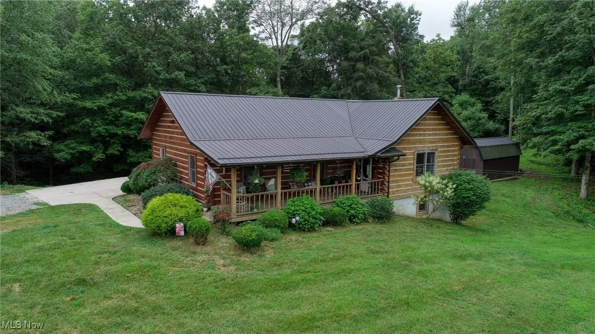 Log home featuring a porch, a front yard, a metal roof, a wooded view, and a standing seam roof