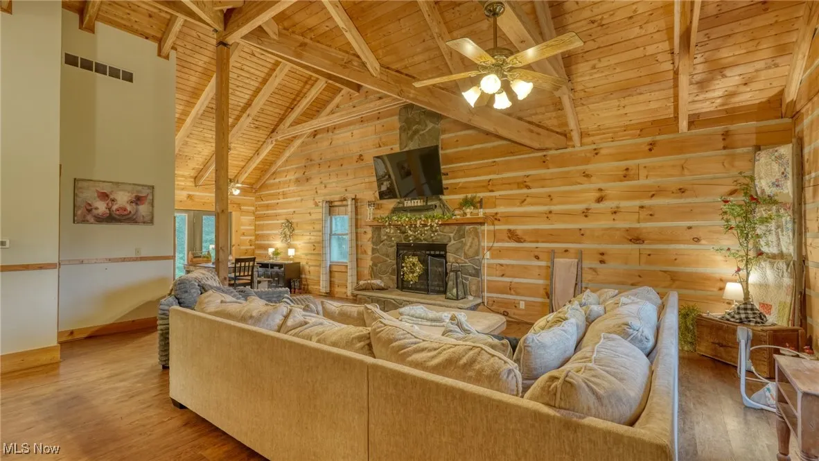 Living room featuring a wood ceiling with exposed beams, high vaulted ceiling, ceiling fan, wood finished floors, and wood walls