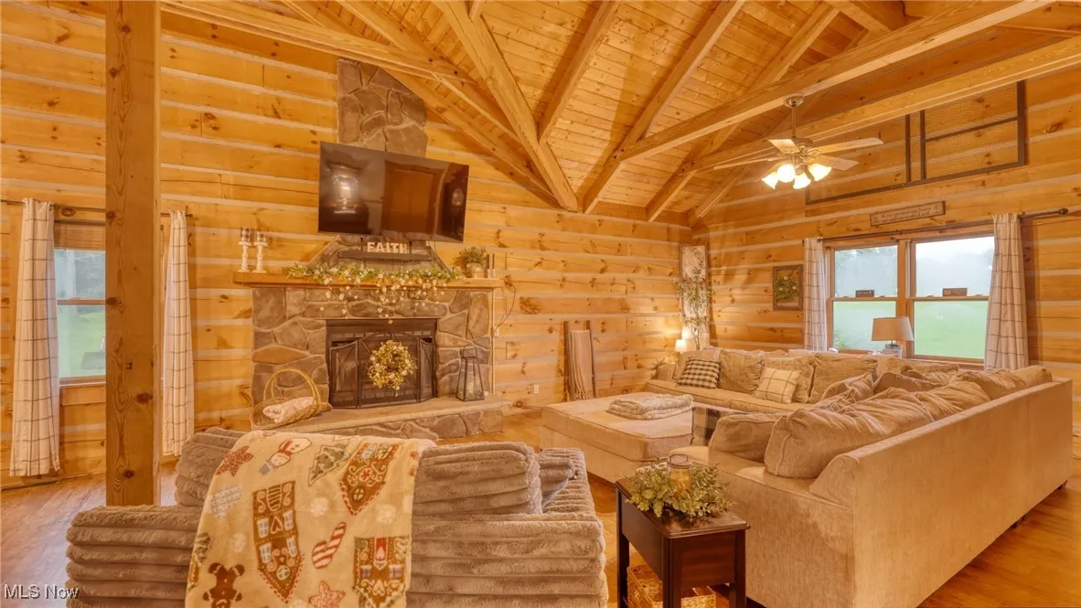 Living area with wood ceiling, wooden walls, wood finished floors, a ceiling fan, and a stone fireplace