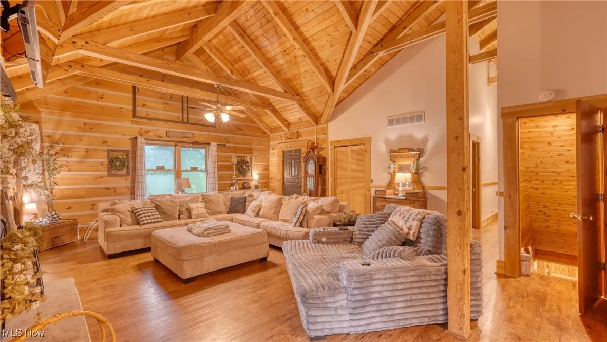 Living area with a wood ceiling with exposed beams, high vaulted ceiling, wood finished floors, and ceiling fan