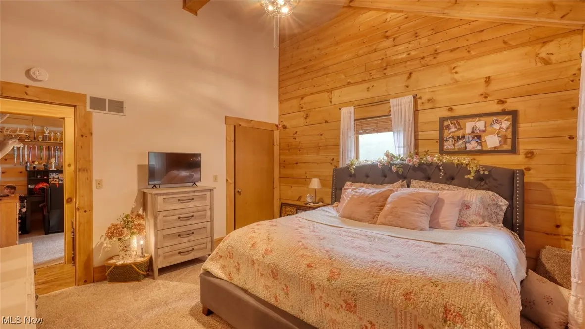 Bedroom featuring light colored carpet, a high ceiling, and wood walls