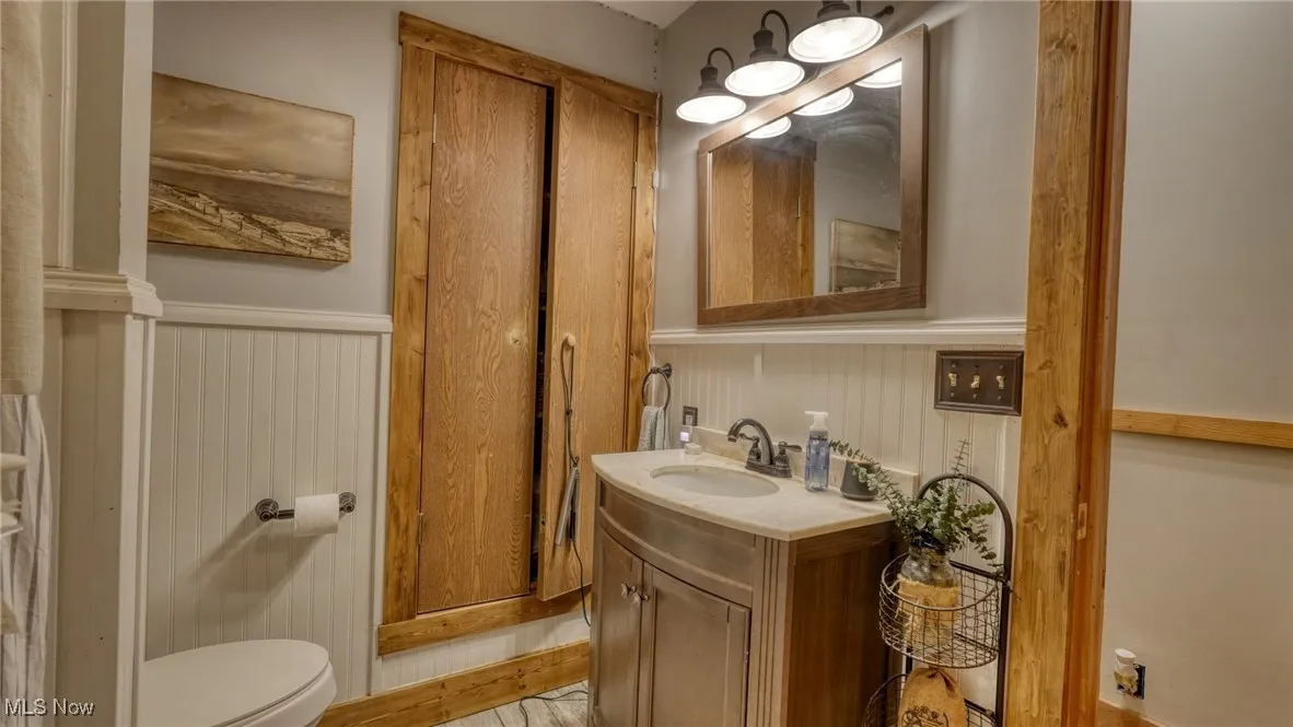 Half bathroom with wainscoting, vanity, and wood finished floors