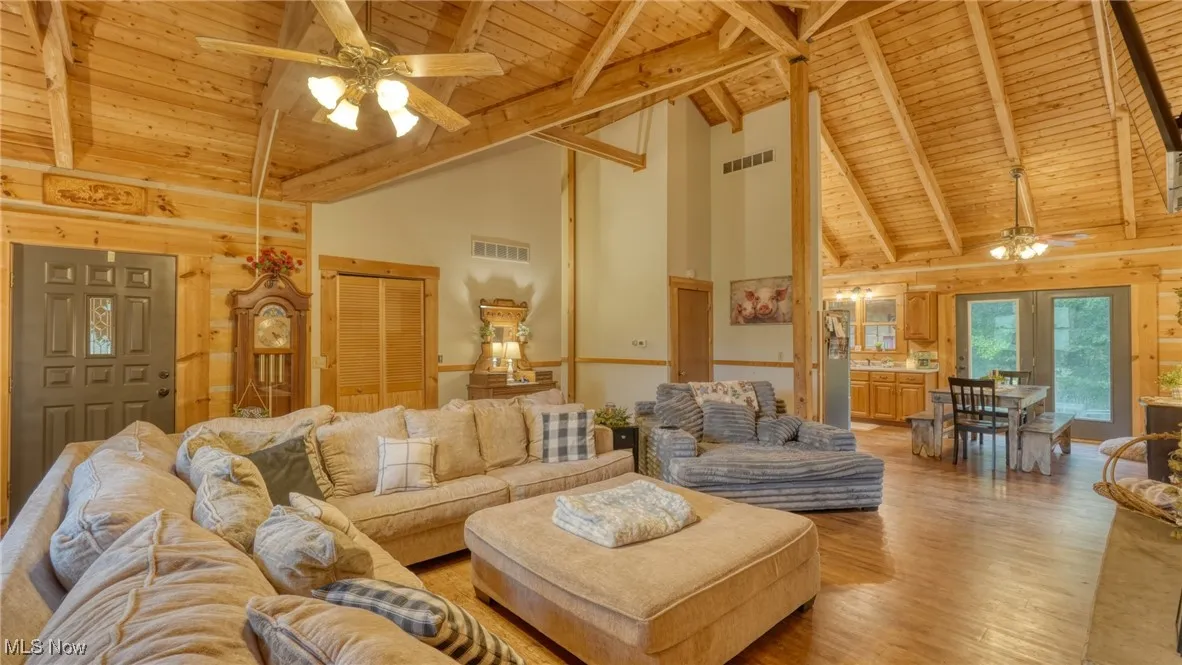 Living room featuring a ceiling fan, a wood ceiling with exposed beams, high vaulted ceiling, light wood-style flooring, and wooden walls