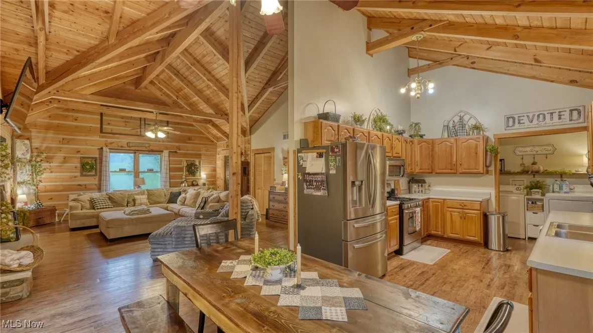 Kitchen featuring a wood ceiling with exposed beams, washing machine and dryer, stainless steel appliances, high vaulted ceiling, and light wood-style floors