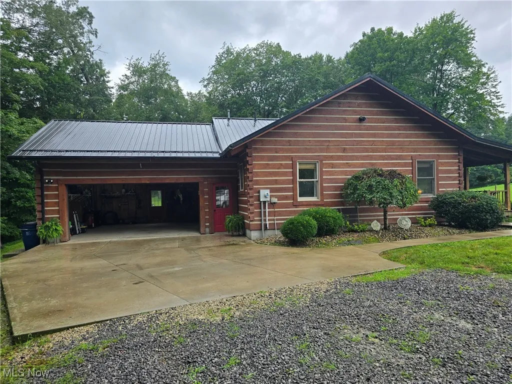 Log cabin featuring concrete driveway, a metal roof, a garage, and log exterior