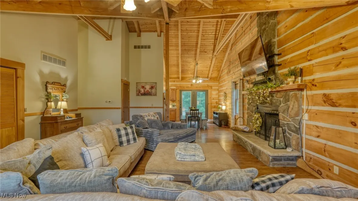Living area featuring high vaulted ceiling, wood finished floors, a wood ceiling with exposed beams, french doors, and a stone fireplace