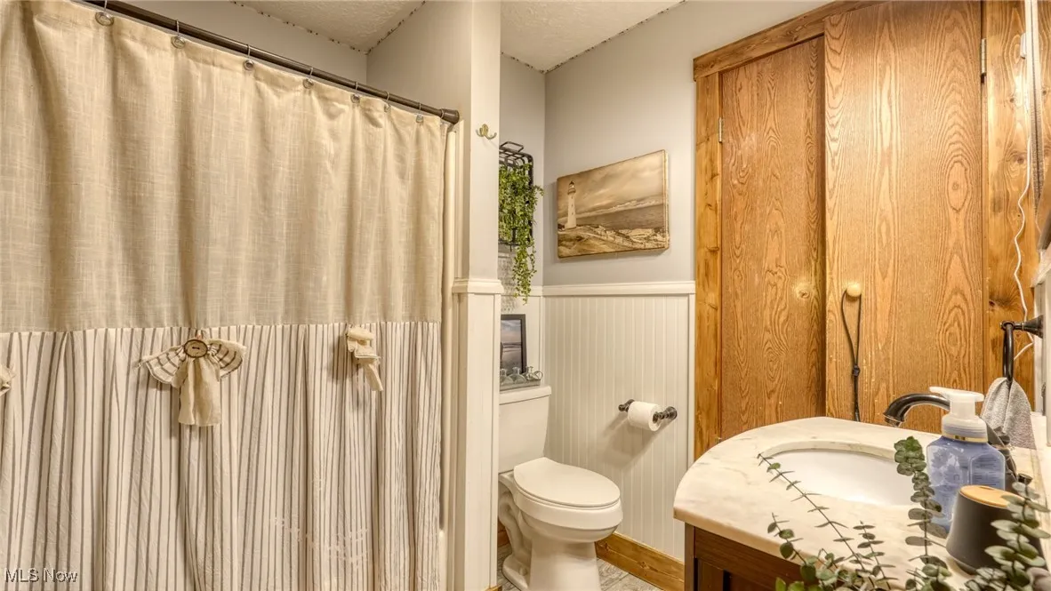 Bathroom with wainscoting, vanity, a textured ceiling, and a shower with shower curtain