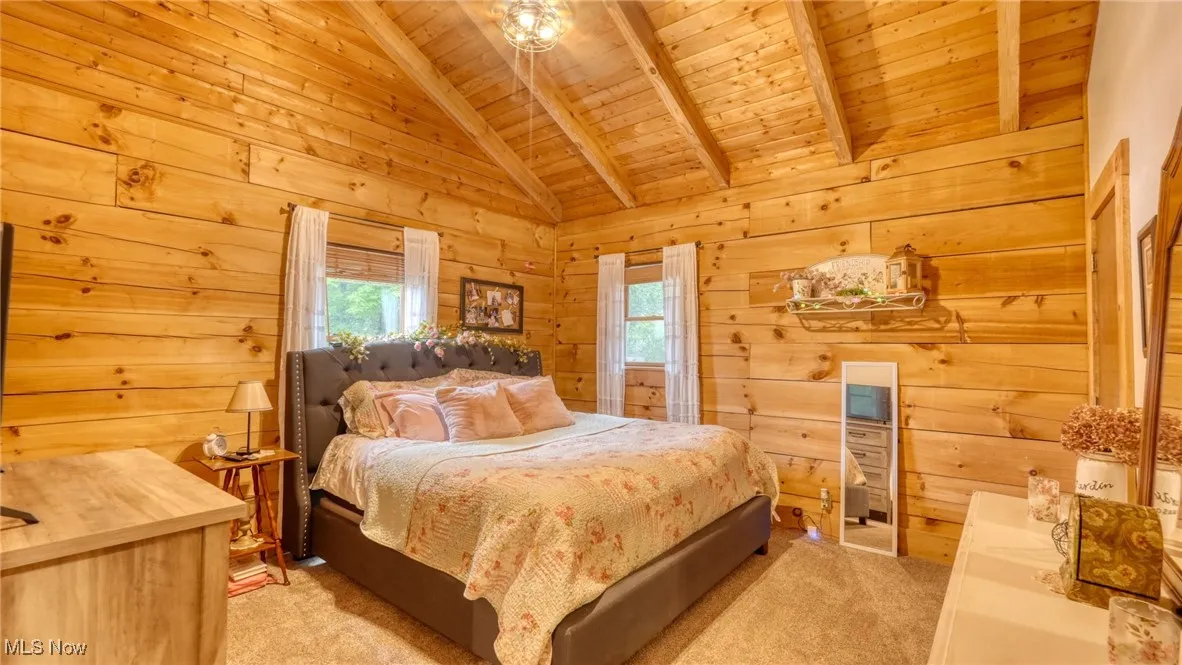 Bedroom featuring wooden ceiling, multiple windows, light carpet, and wood walls