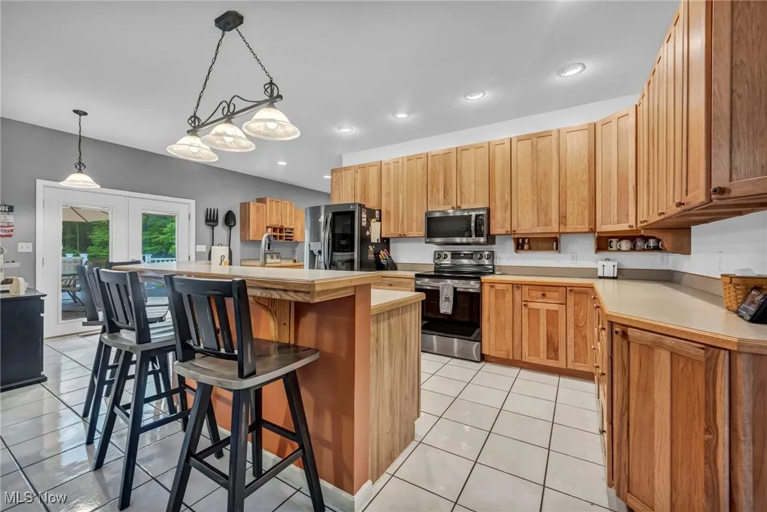 Kitchen with stainless steel appliances, a breakfast bar, light countertops, light tile patterned flooring, and a center island with sink