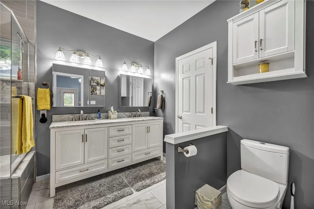 Full bathroom featuring marble look tile flooring, double vanity, and tiled shower