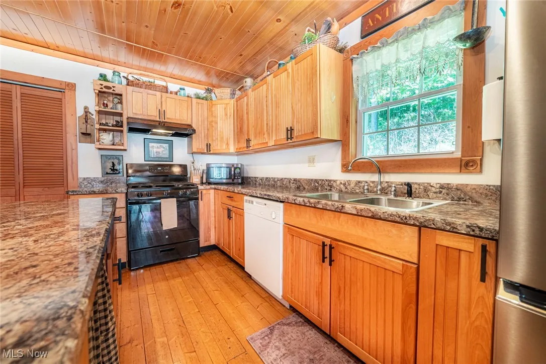 Kitchen featuring appliances with stainless steel finishes, wood ceiling, under cabinet range hood, light wood-style floors, and dark stone countertops