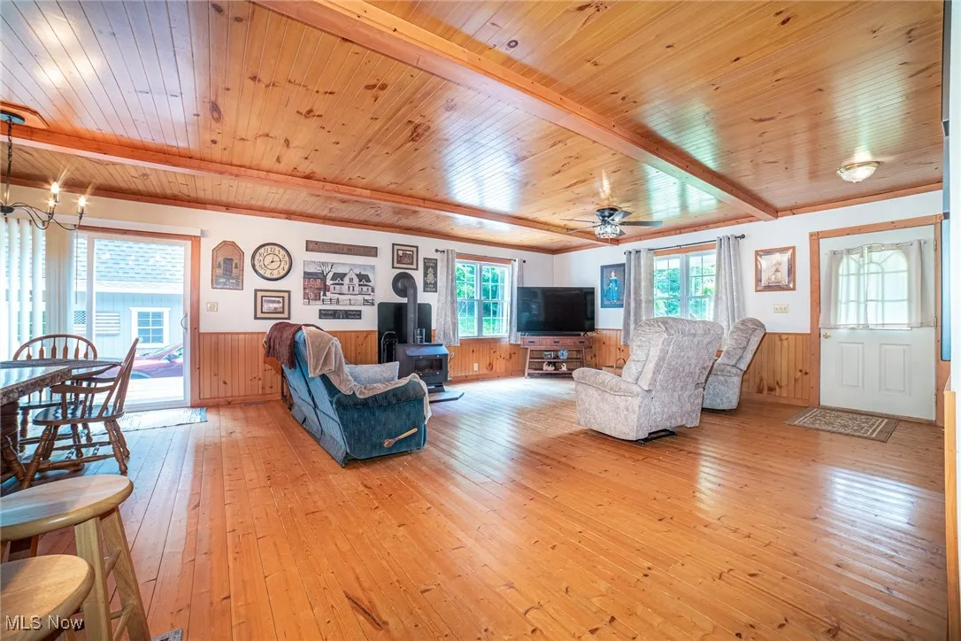 Living area with a wainscoted wall, a wood stove, wooden ceiling, light wood-style floors, and a chandelier