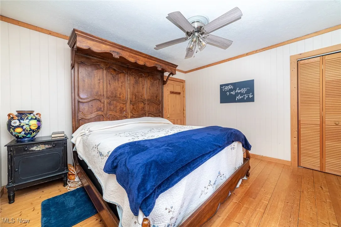 Bedroom featuring light wood finished floors, crown molding, a ceiling fan, and wood walls