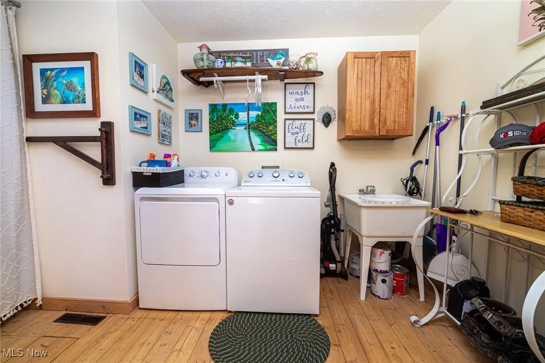 Laundry room with washing machine and clothes dryer, light wood-style flooring, and cabinet space