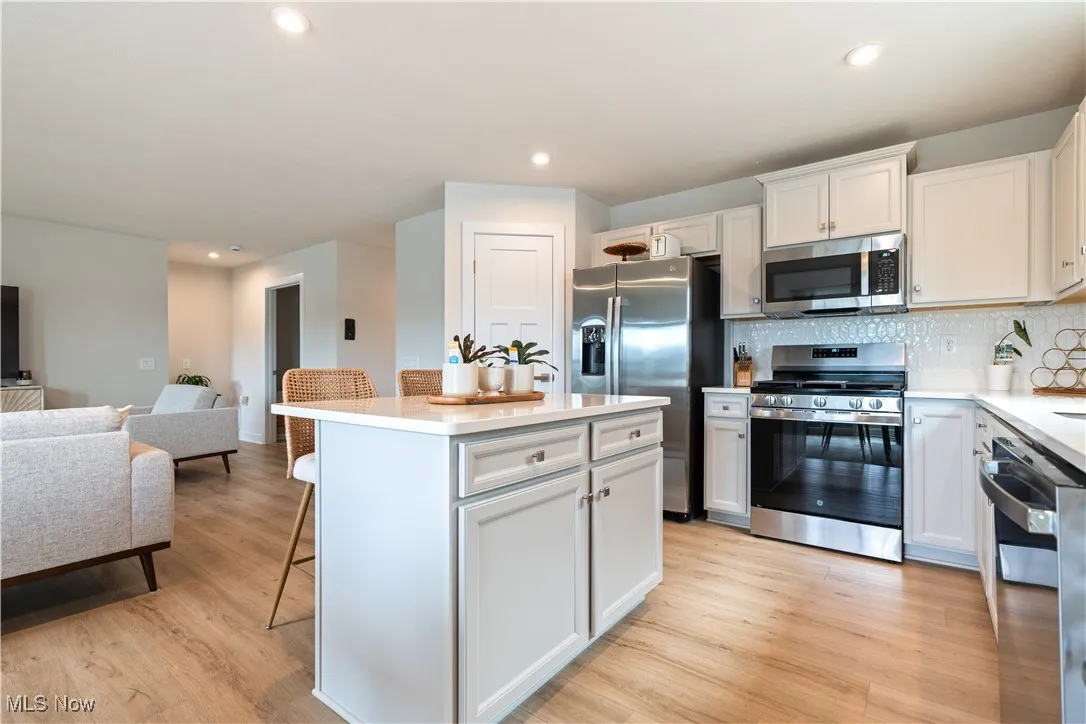 Kitchen featuring appliances with stainless steel finishes, a kitchen island, open floor plan, a breakfast bar, and light wood-style flooring