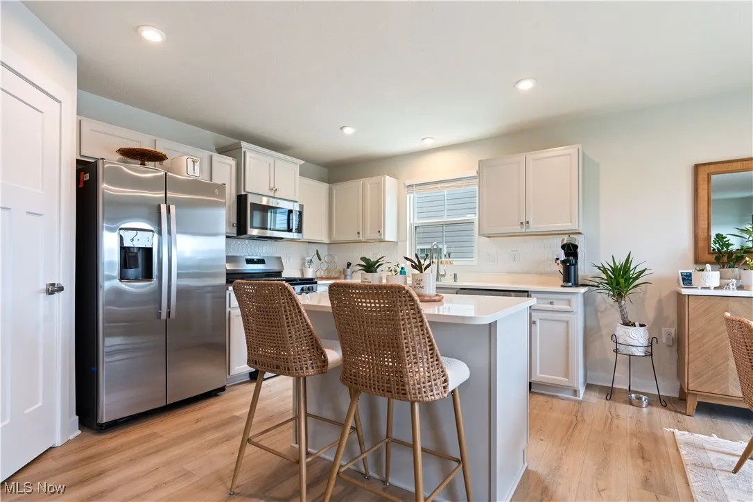 Kitchen with appliances with stainless steel finishes, light wood-style floors, decorative backsplash, a kitchen island, and recessed lighting
