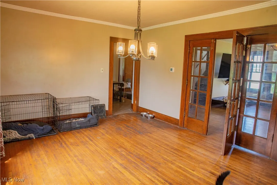 Unfurnished room with french doors, wood finished floors, a chandelier, and ornamental molding