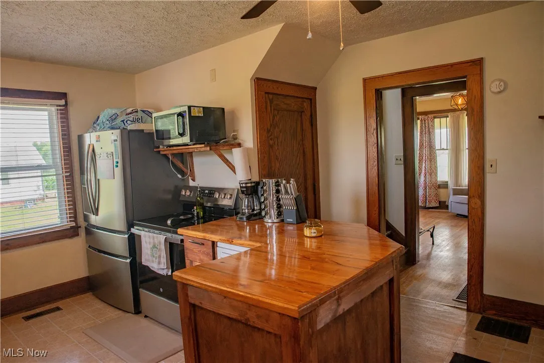 Kitchen with butcher block counters, appliances with stainless steel finishes, a textured ceiling, healthy amount of natural light, and ceiling fan