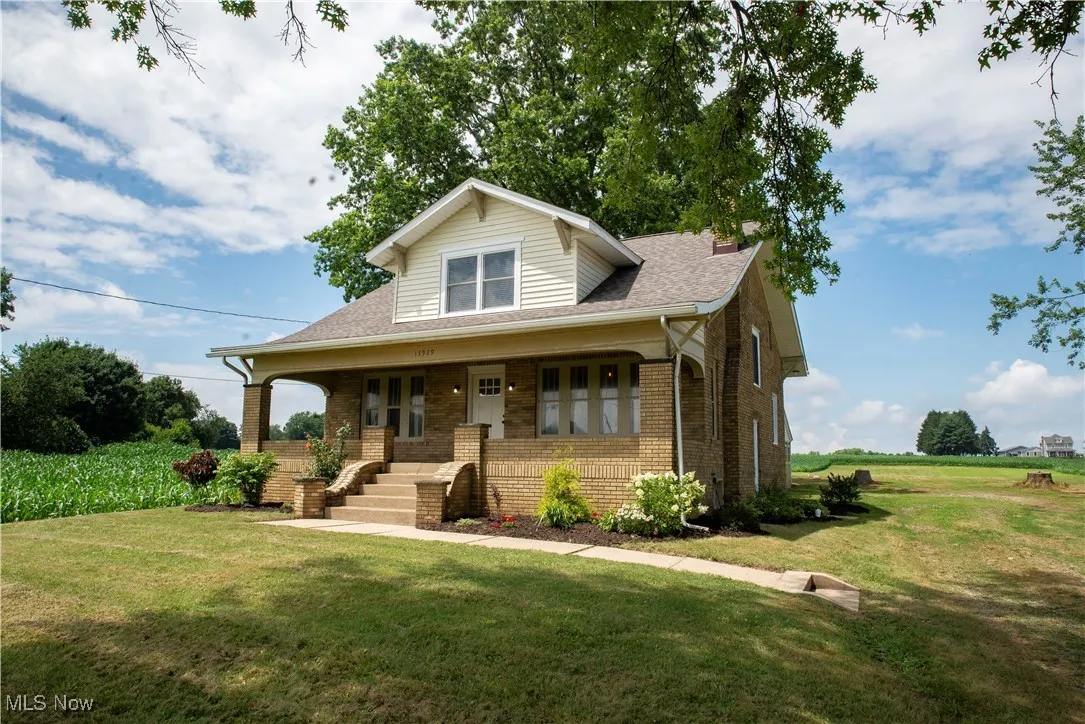 Bungalow-style house featuring brick siding, a front yard, covered porch, and a shingled roof