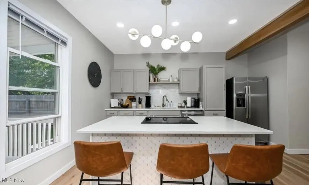 Kitchen with stainless steel refrigerator with ice dispenser, light wood-style floors, light countertops, a breakfast bar area, and recessed lighting