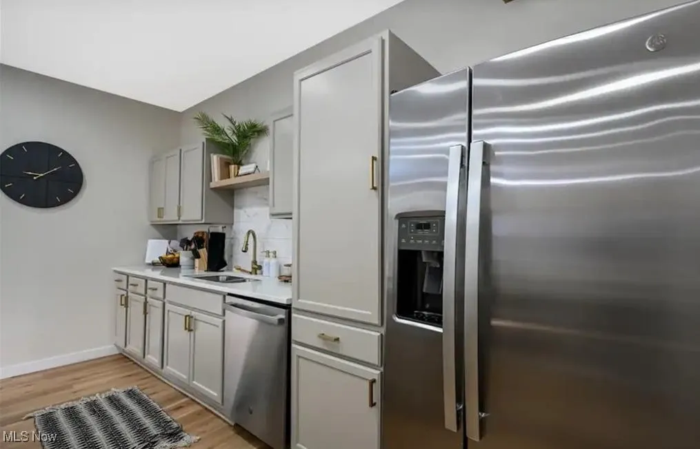 Kitchen with stainless steel appliances, light wood-style floors, gray cabinetry, light countertops, and open shelves