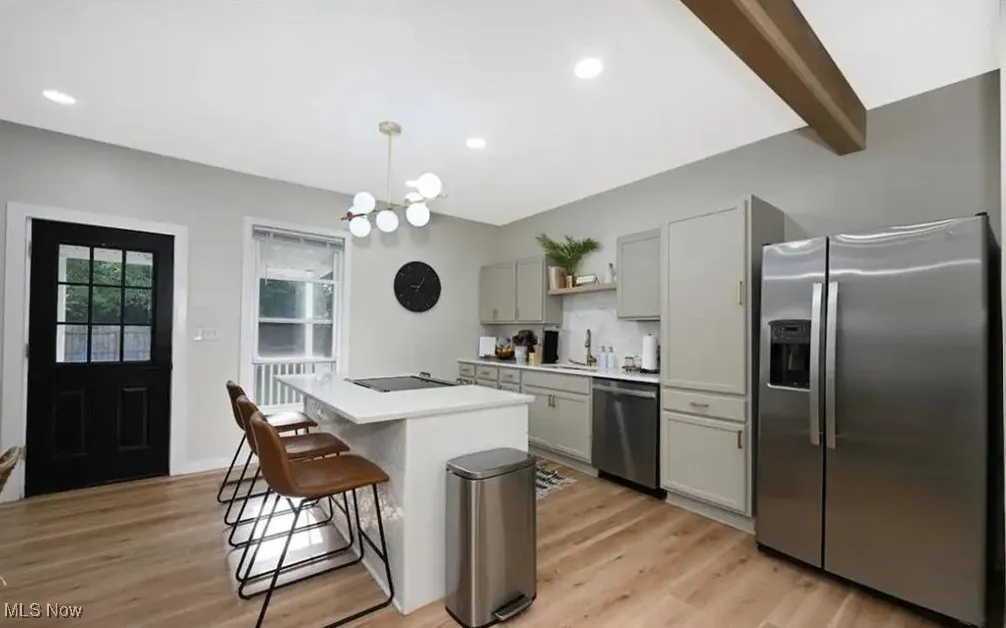 Kitchen featuring stainless steel fridge, gray cabinets, a breakfast bar area, light wood-style flooring, and a chandelier