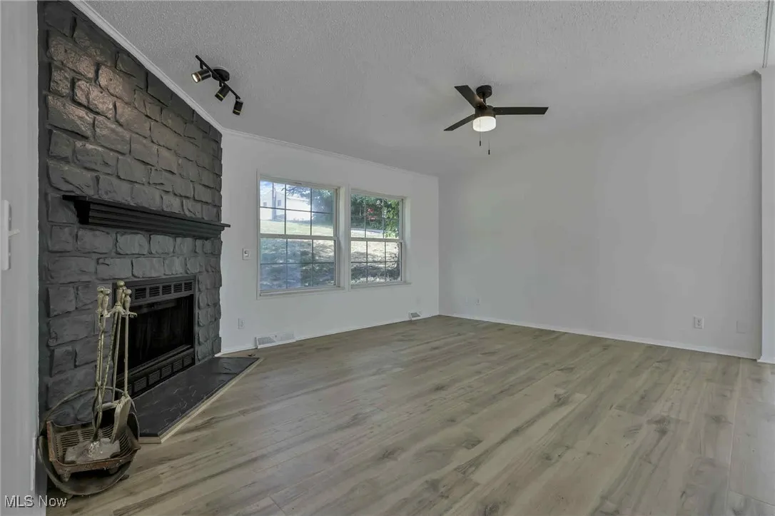 Unfurnished living room with a textured ceiling, a ceiling fan, a fireplace, wood finished floors, and rail lighting