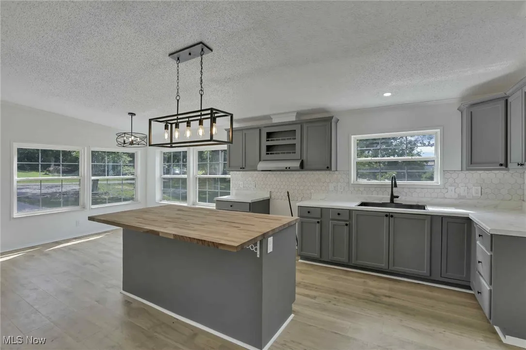 Kitchen with gray cabinetry, wood counters, a textured ceiling, backsplash, and a chandelier