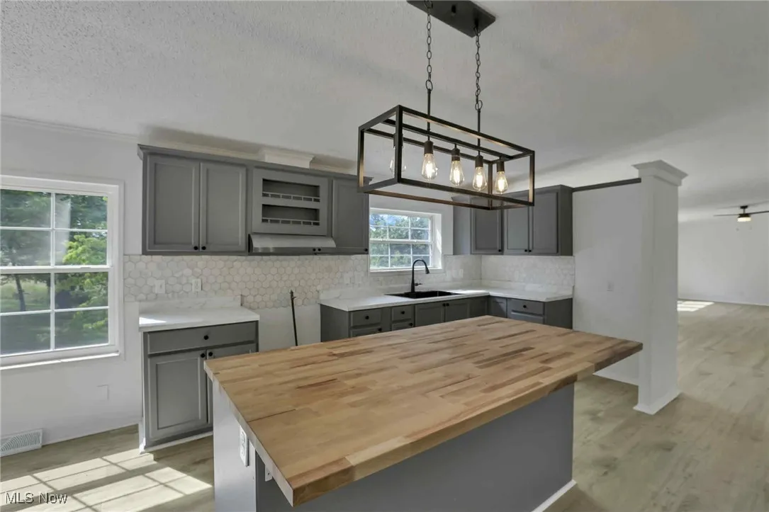 Kitchen with gray cabinets, butcher block countertops, backsplash, pendant lighting, and light wood-type​​‌​​​​‌​​‌‌​‌‌​​​‌‌​‌​‌​‌​​​‌​​ flooring