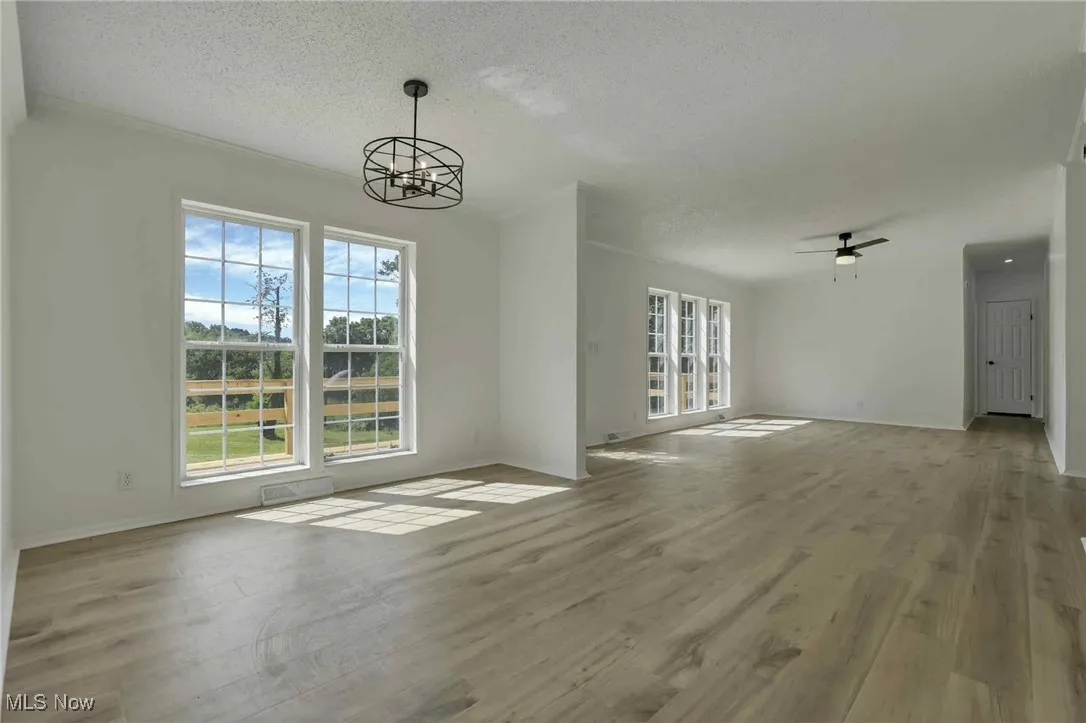 Unfurnished living room with a chandelier, a textured ceiling, wood finished floors, and ceiling fan