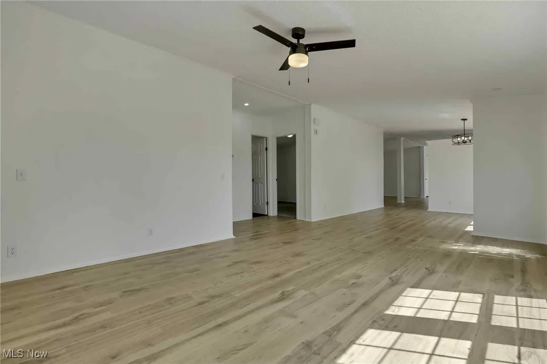 Unfurnished room featuring a ceiling fan, a chandelier, and wood finished floors