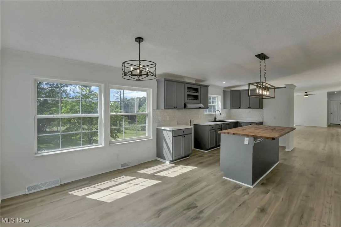 Kitchen featuring butcher block countertops, gray cabinets, a chandelier, decorative backsplash, and light wood finished floors