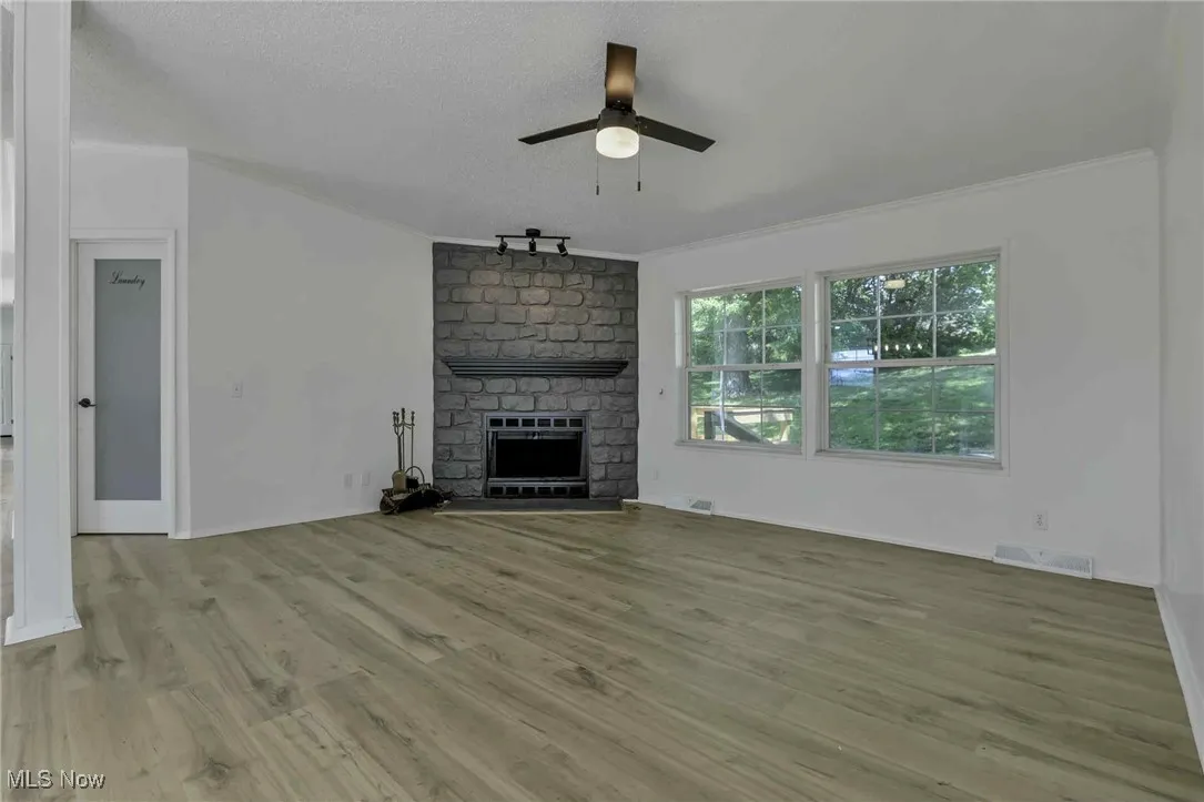 Unfurnished living room with crown molding, ceiling fan, a fireplace, wood finished floors, and a textured ceiling