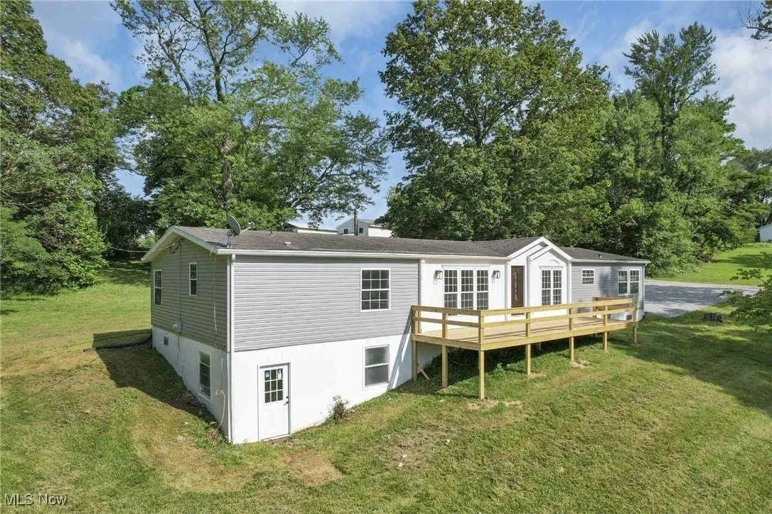 Back of house with a wooden deck, a yard, roof with shingles, and view of scattered trees