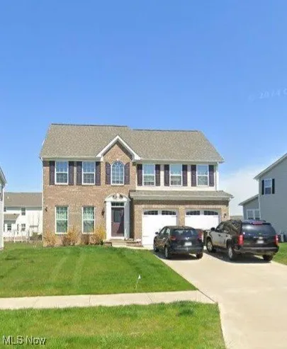 Colonial home featuring driveway, an attached garage, and a front lawn