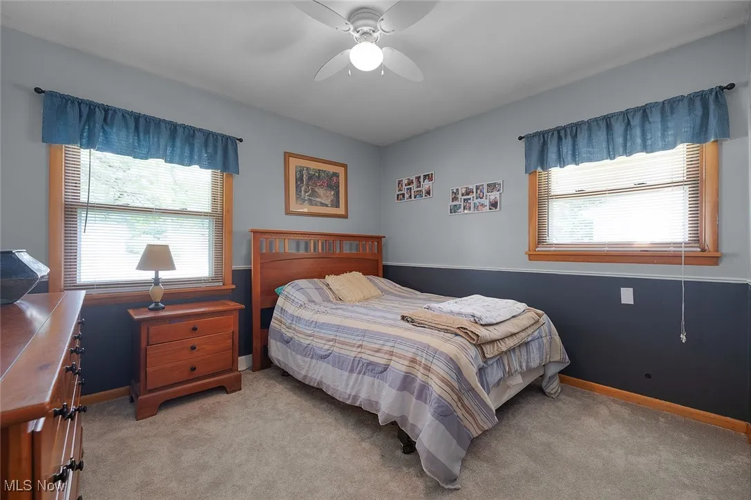 Bedroom featuring light colored carpet, multiple windows, and a ceiling fan