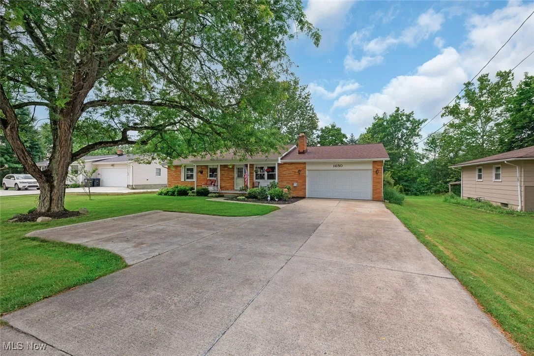 Single story home featuring brick siding, a front lawn, driveway, an attached garage, and a chimney