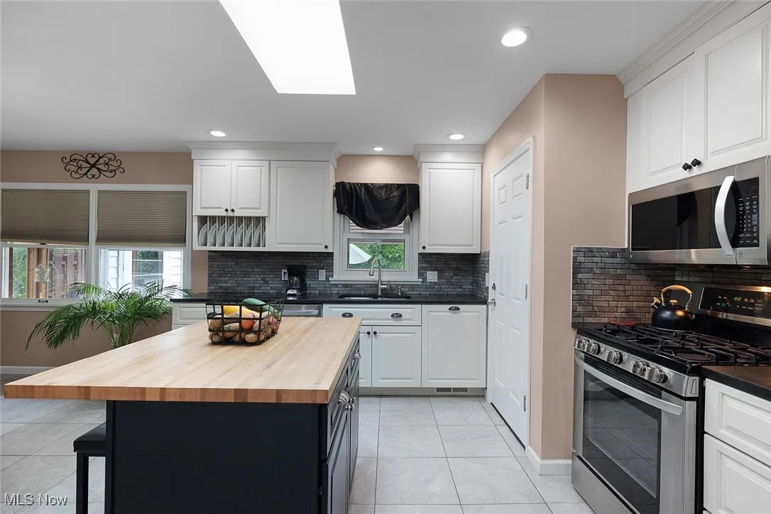 Kitchen featuring wood counters, appliances with stainless steel finishes, a kitchen bar, white cabinets, and recessed lighting