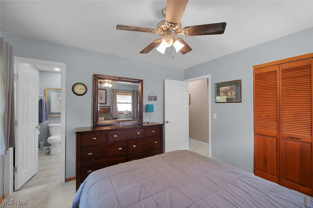 Bedroom with a closet, light carpet, ceiling fan, and ensuite bath
