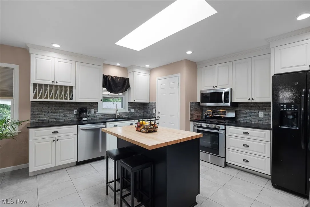 Kitchen with wood counters, appliances with stainless steel finishes, light tile patterned floors, white cabinetry, and tasteful backsplash