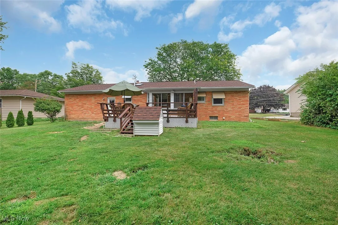 Back of house featuring brick siding, a deck, and a lawn