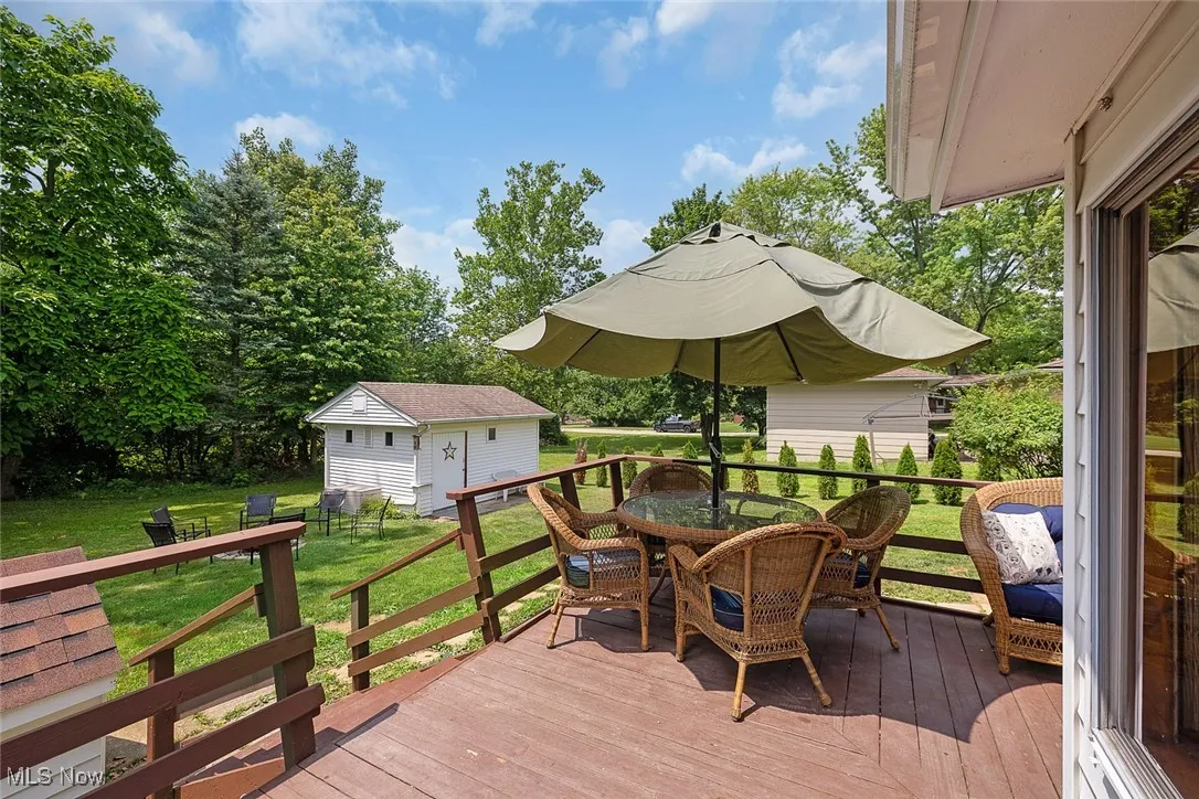 Wooden terrace featuring outdoor dining space, an outdoor structure, and a lawn