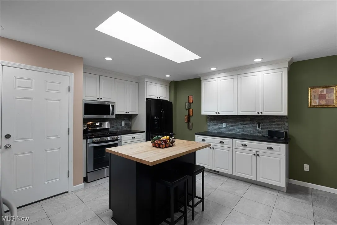 Kitchen featuring wood counters, a skylight, appliances with stainless steel finishes, white cabinets, and recessed lighting