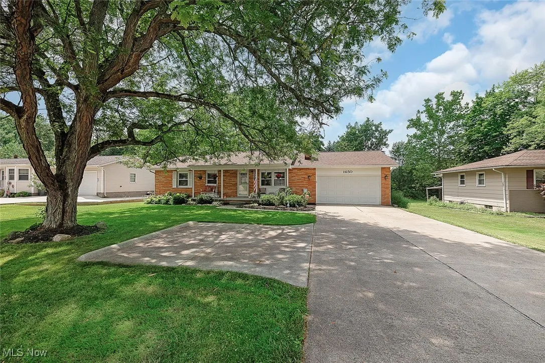 Single story home featuring an attached garage, a front lawn, driveway, and brick siding
