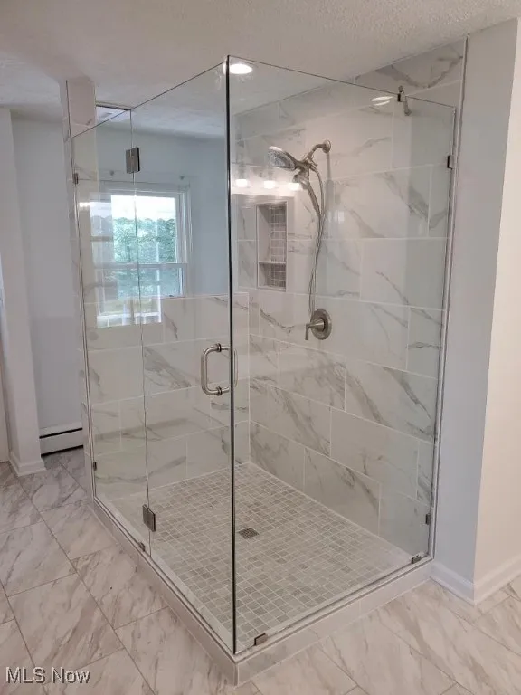 Full bath with marble look tile flooring, a shower stall, a baseboard radiator, and a textured ceiling