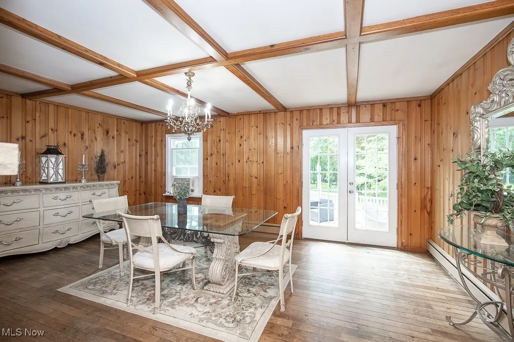 Dining space featuring a baseboard heating unit, wood walls, a chandelier, french doors, and hardwood / wood-style floors