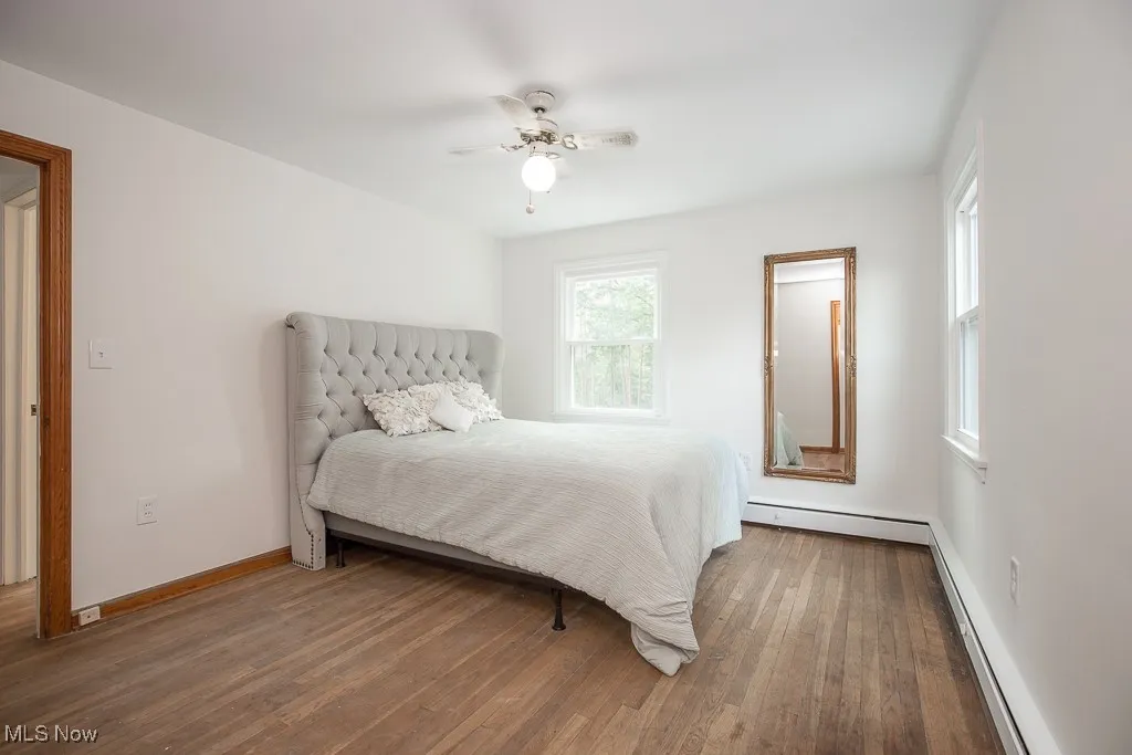 Bedroom with baseboard heating, wood finished floors, a baseboard radiator, and a ceiling fan